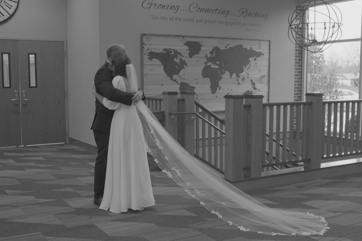 Bride and groom share private moment in church hallway with world map wall art.