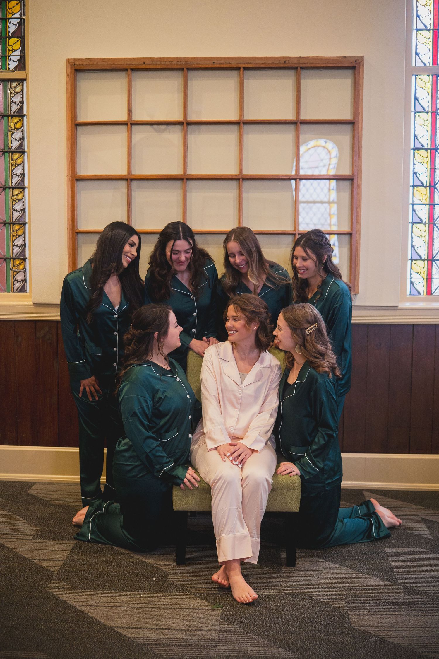 Wedding party in matching dark robes gathered around someone in white in a church setting.