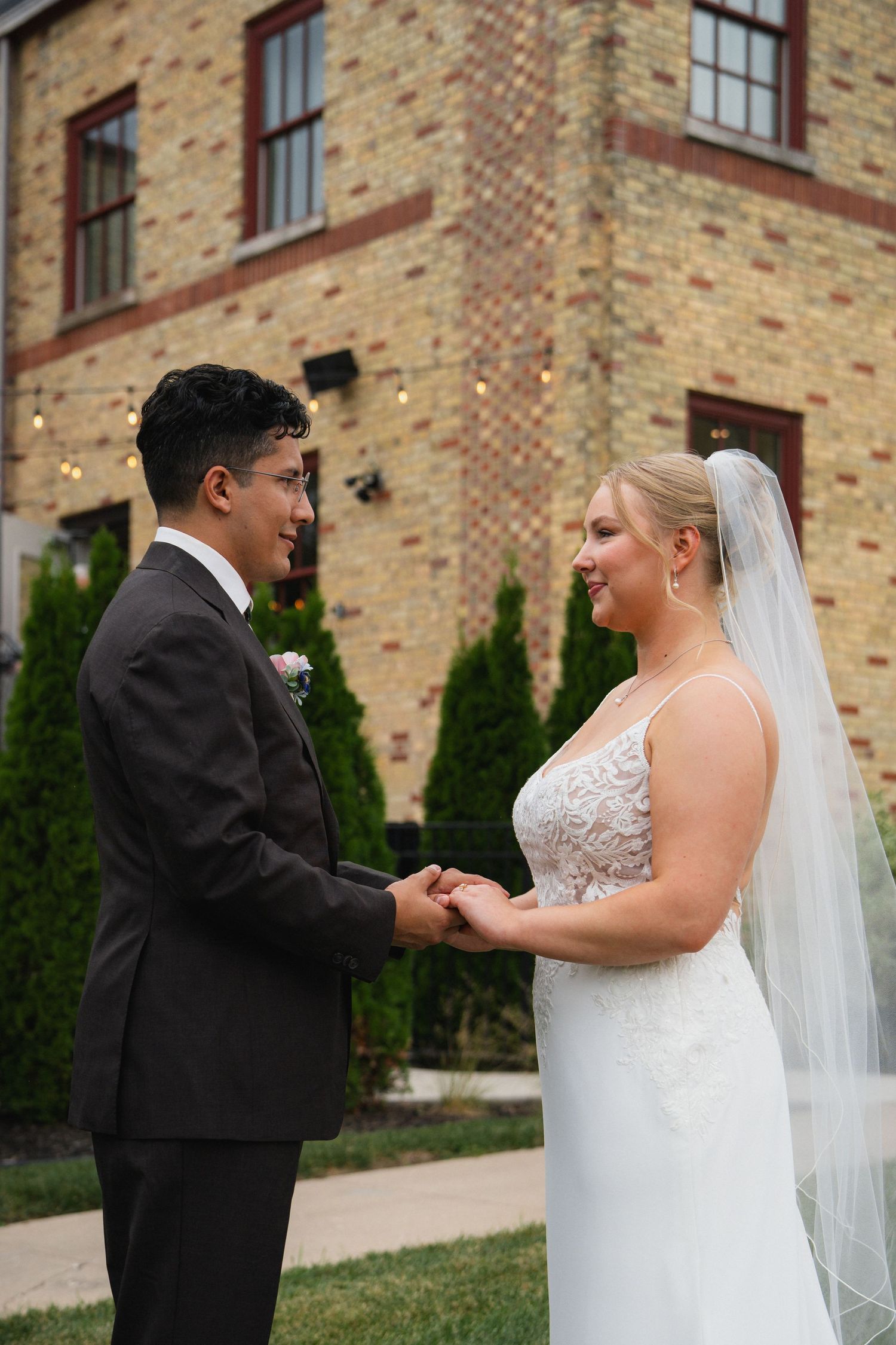 A couple in wedding attire holding hands in front of a brick building.