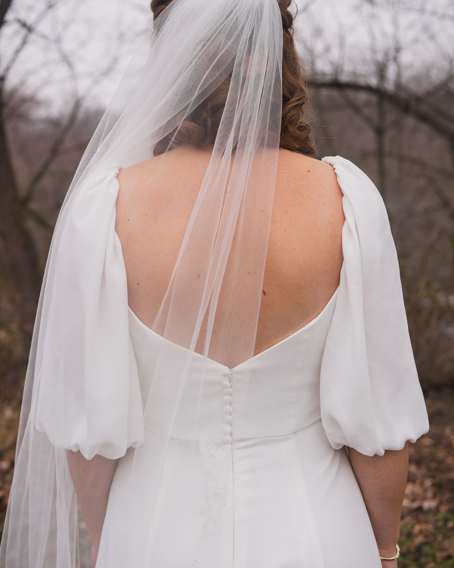 Close-up of white wedding dress back detail showing buttons and puff sleeves with flowing veil.