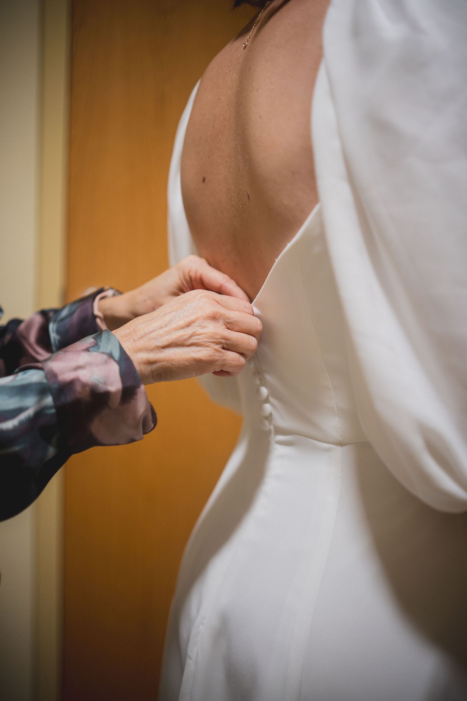 Close-up shot of hands buttoning up a white wedding dress.