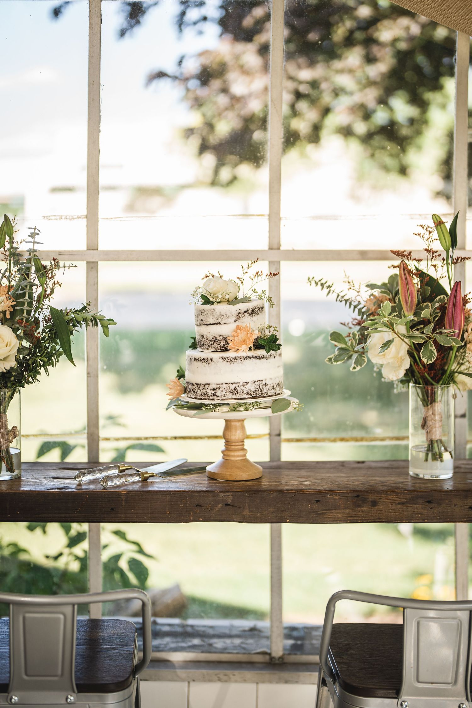 Rustic window display with wedding cakes and floral arrangements on wooden shelves.
