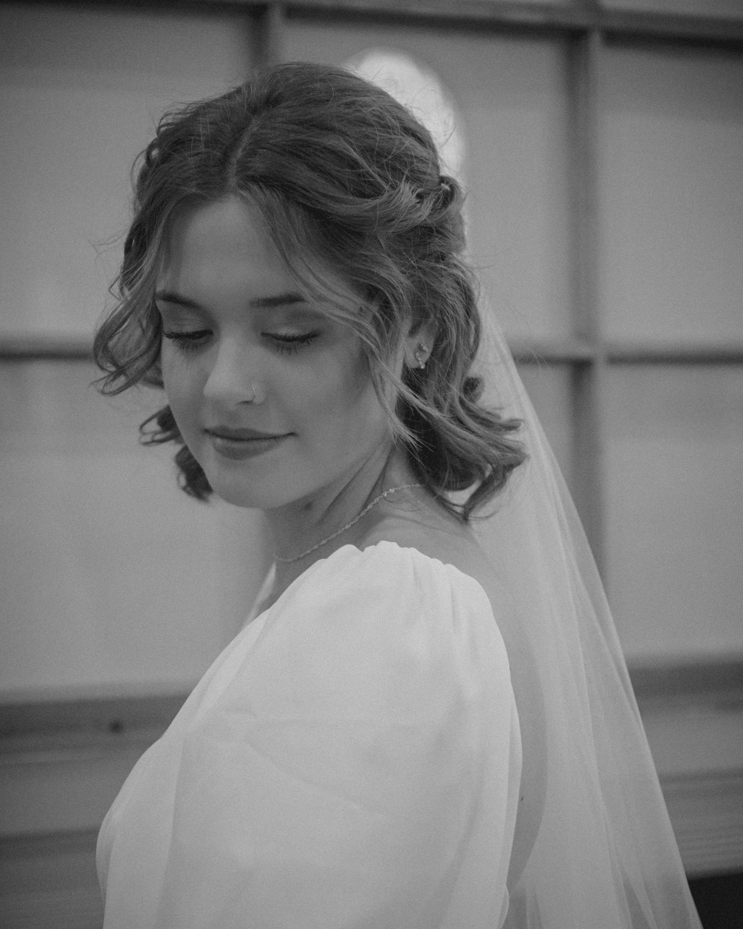 A bride in a white dress and veil poses with a soft smile in black and white.