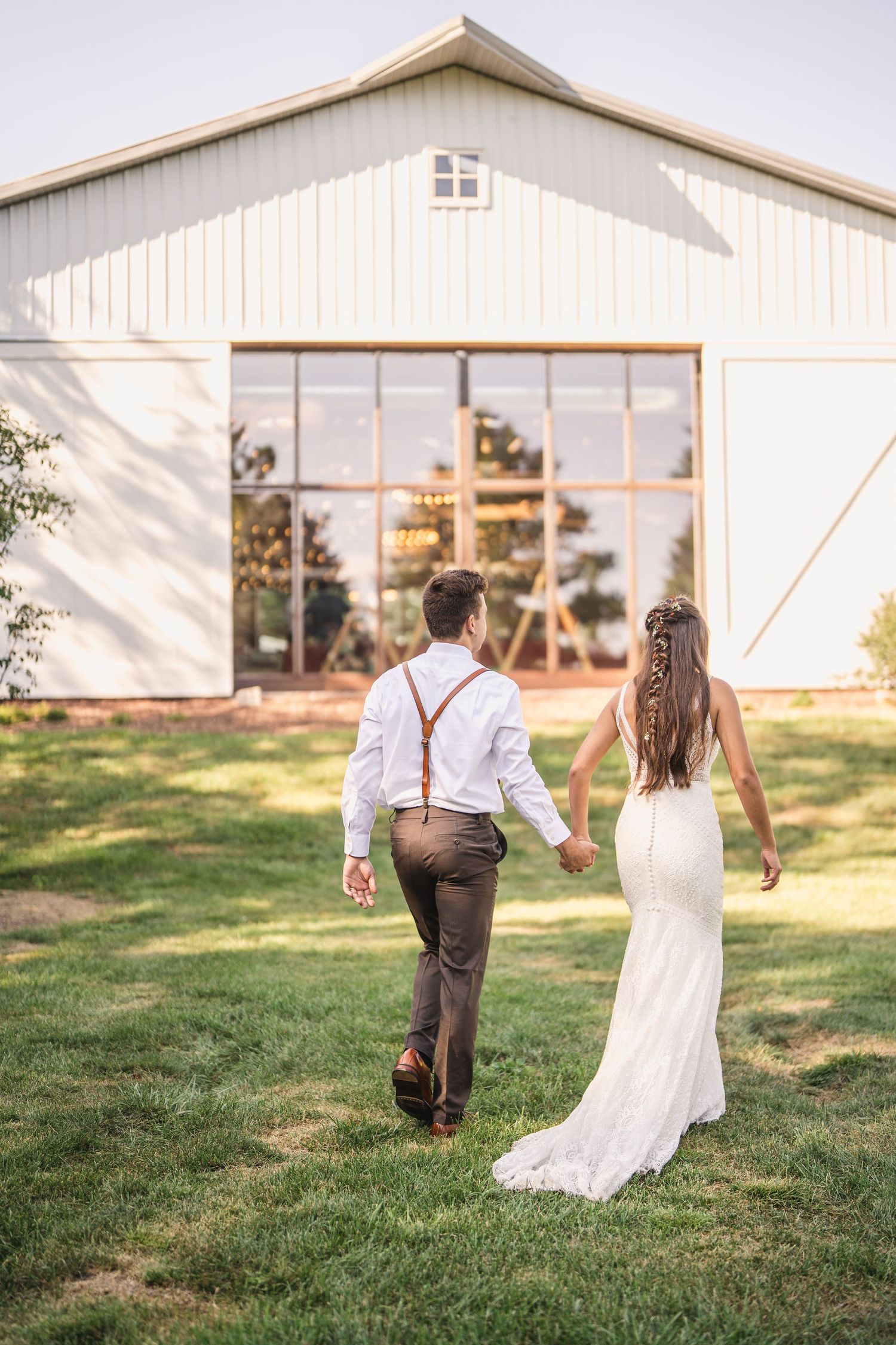 Newlyweds walking together on a grassy lawn in front of a white barn building.