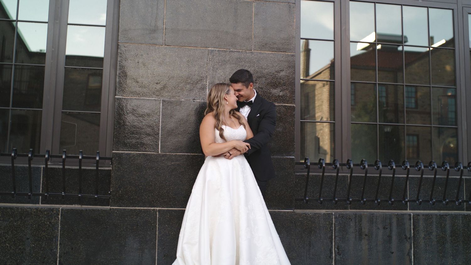 Romantic wedding moment captured against modern glass building exterior.