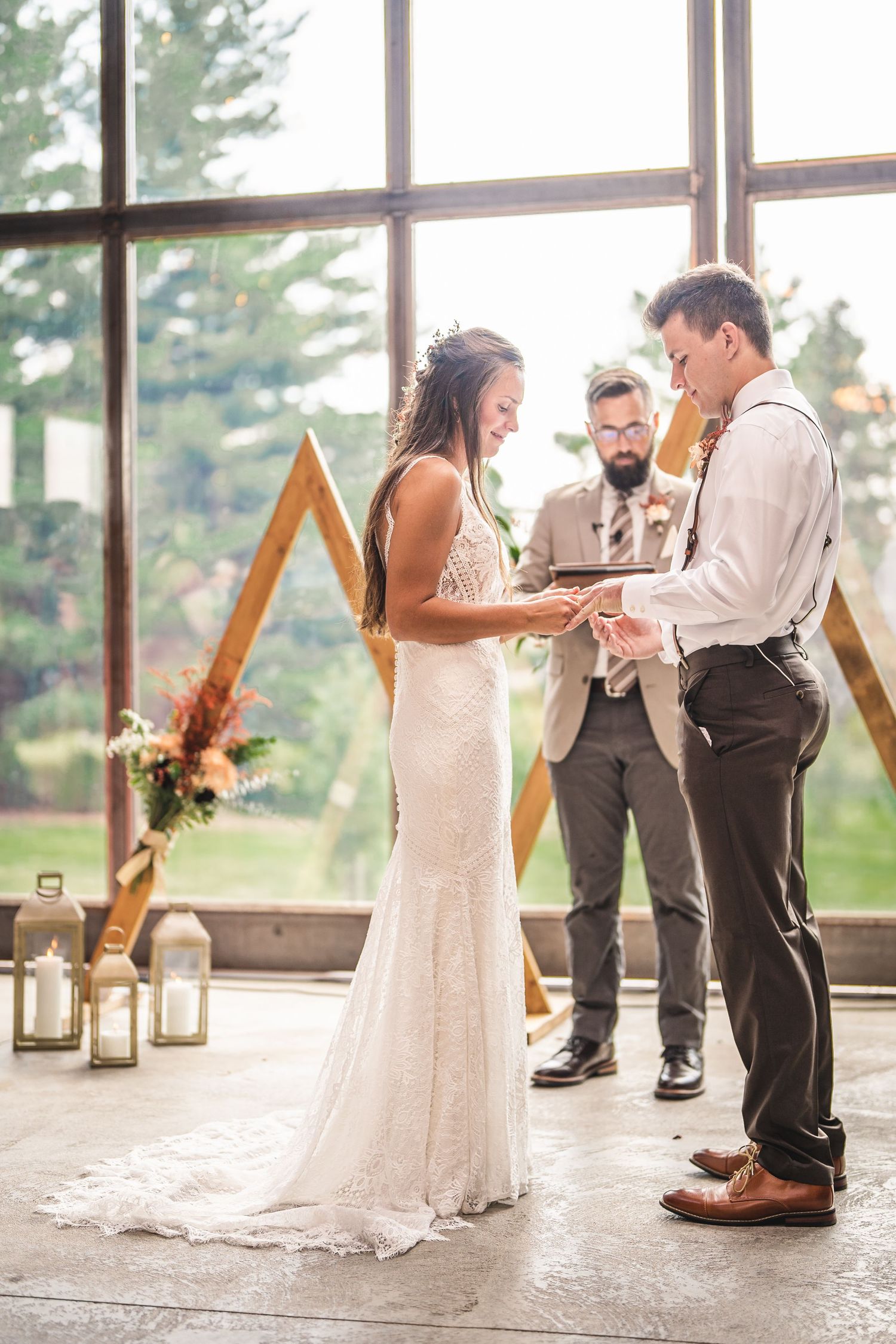 Wedding ceremony with geometric wooden arch backdrop and natural light streaming through large windows.