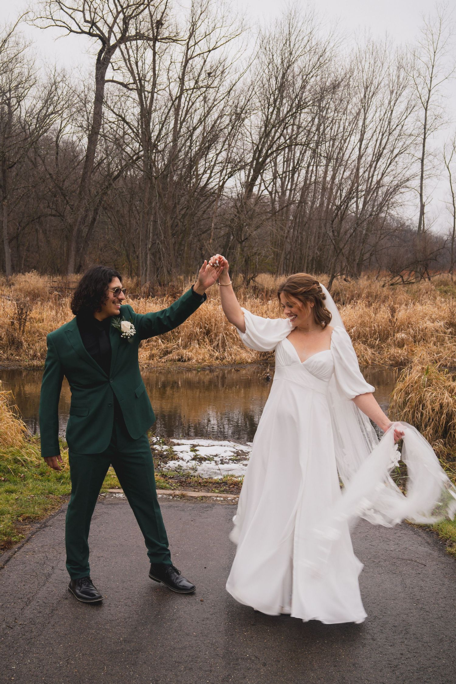 A joyful wedding couple high-fiving on a path with autumn foliage in the background.
