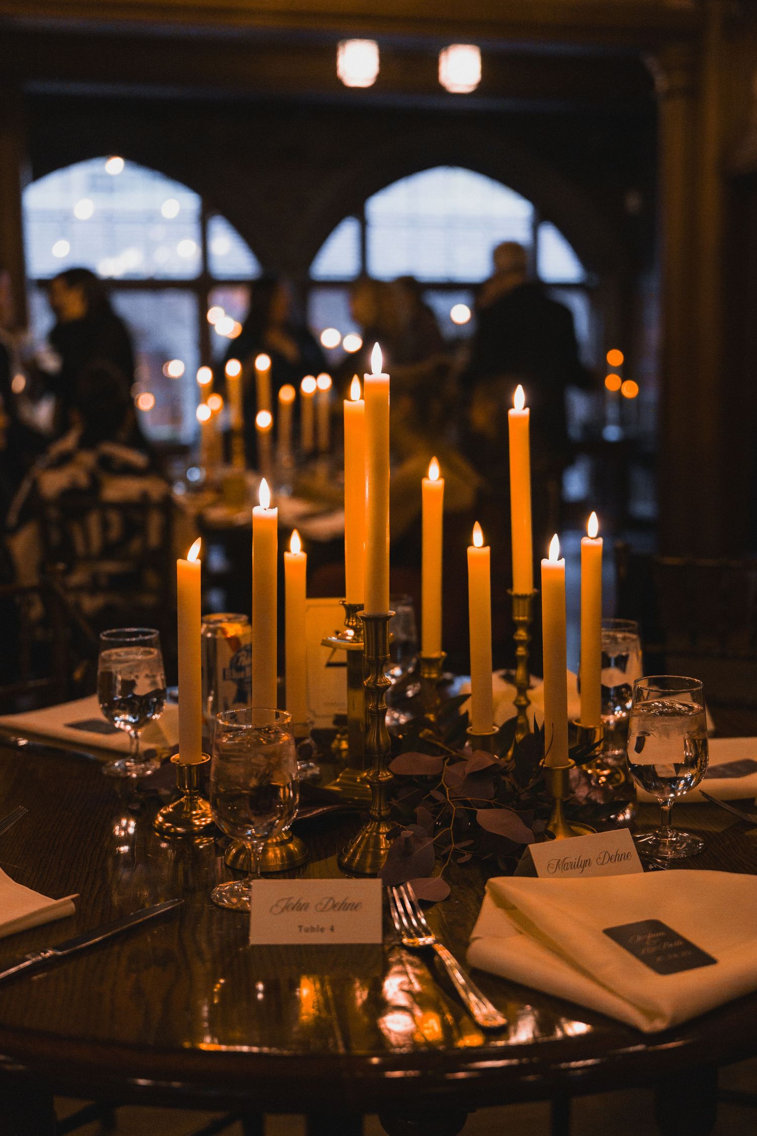 Elegant wedding reception table setting with glowing candles and place settings in dim lighting.