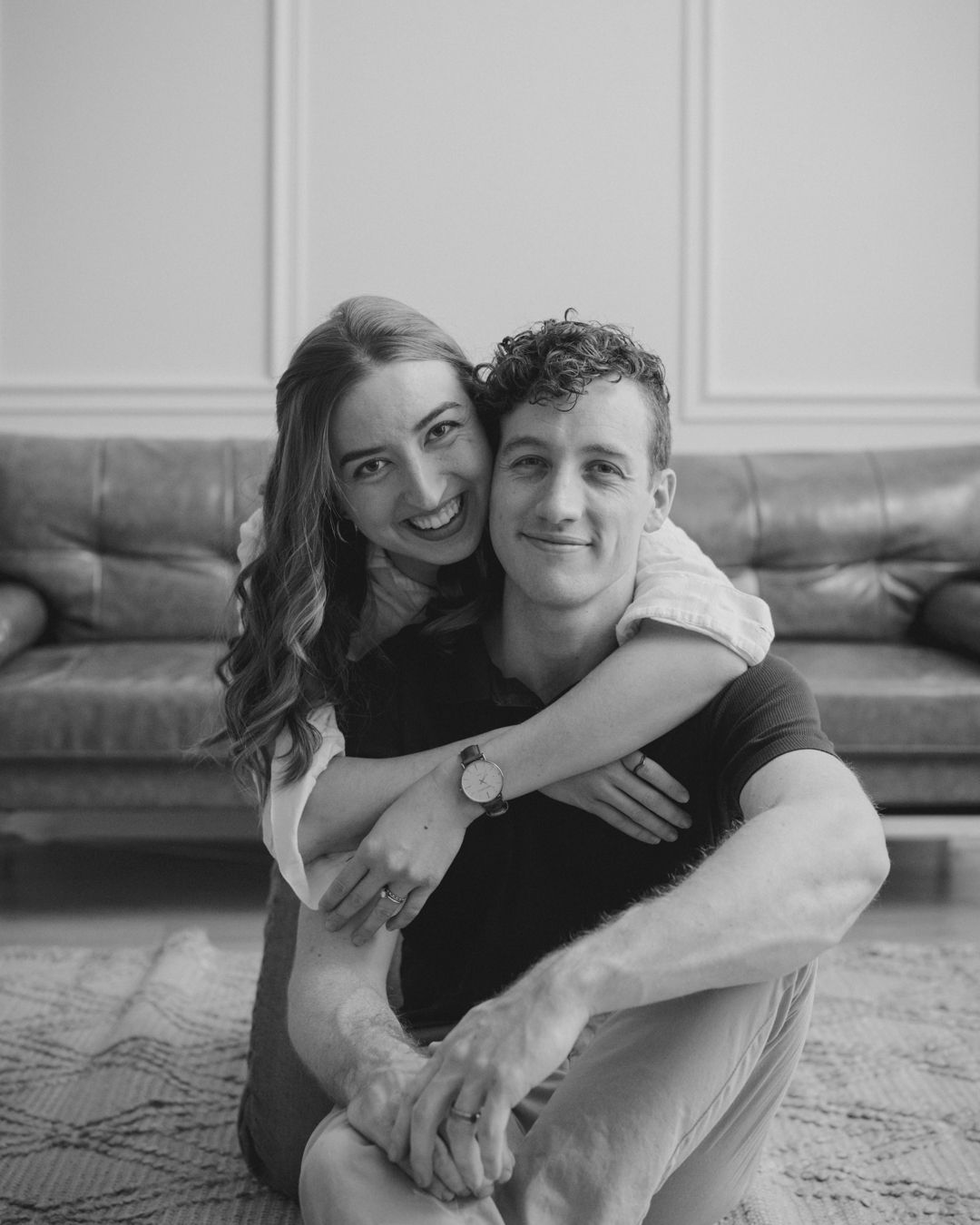 Black and white portrait of couple sharing playful embrace on living room floor.