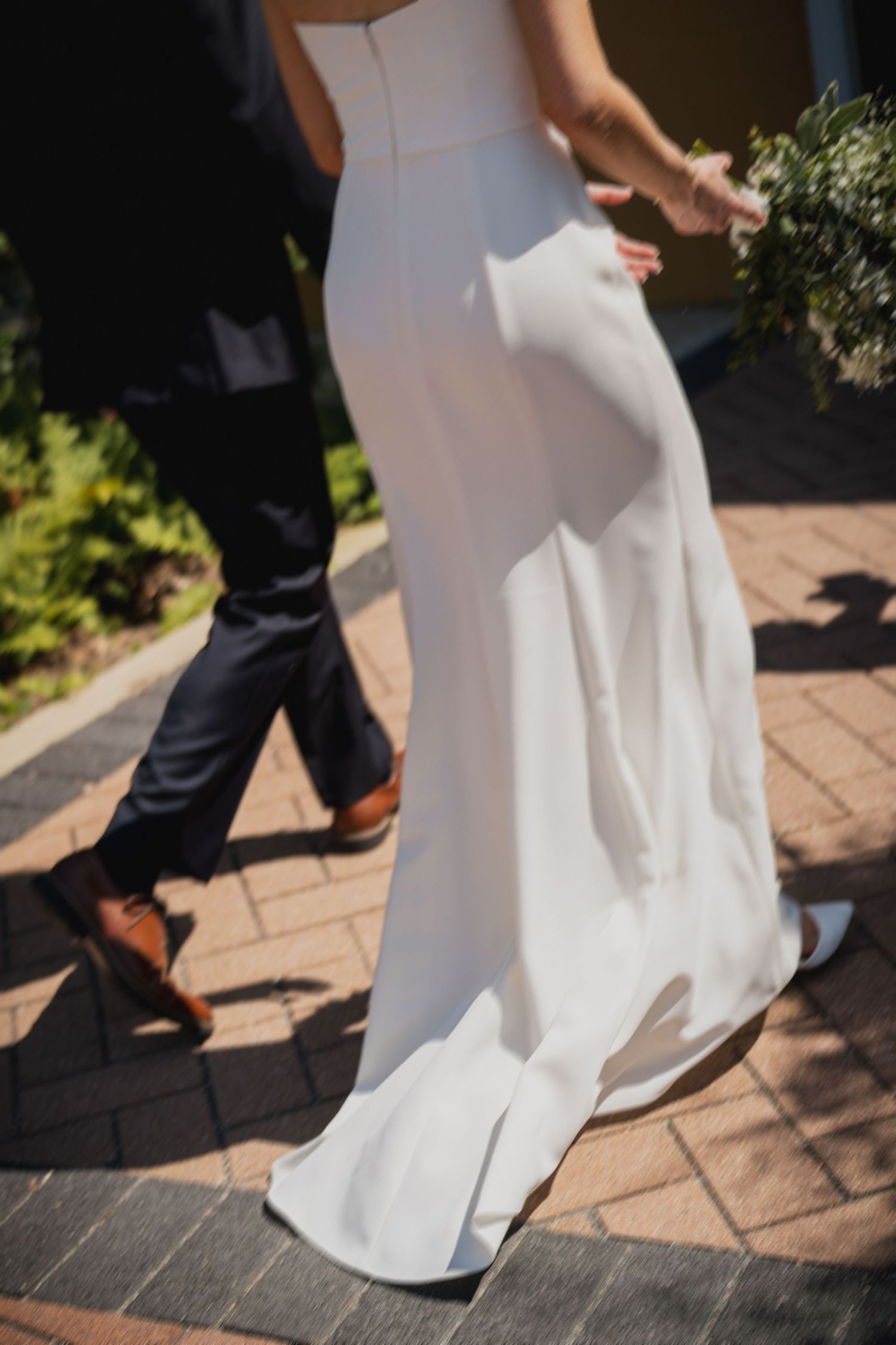 Close-up of formal shoes and wedding dress hem on stone pavement.