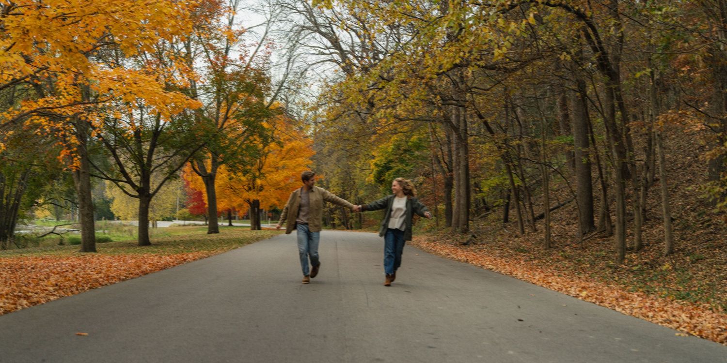 A peaceful autumn scene with two people walking down a leaf-covered path.