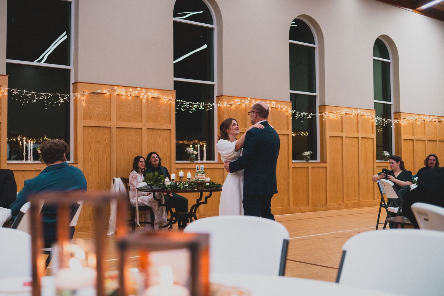 Church hall interior with white walls and wooden paneling decorated with string lights.