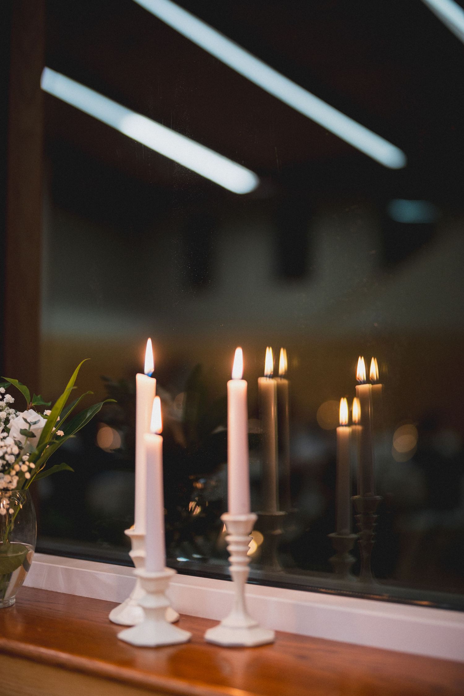 Lit white taper candles in elegant holders create romantic ambiance at wedding reception.