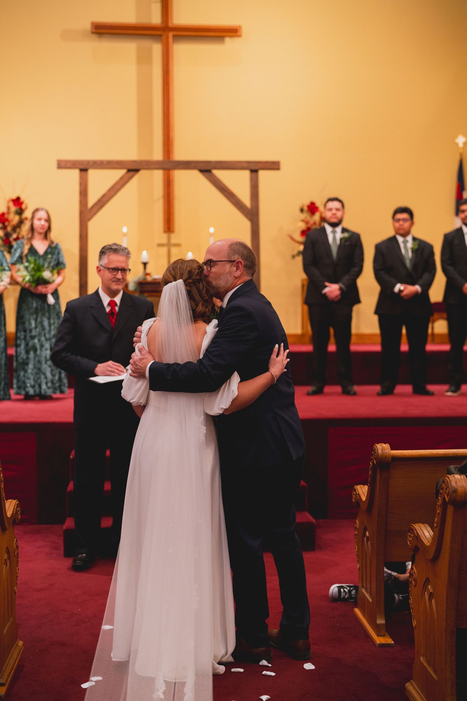 Wedding ceremony in progress with couple at altar under wooden cross.