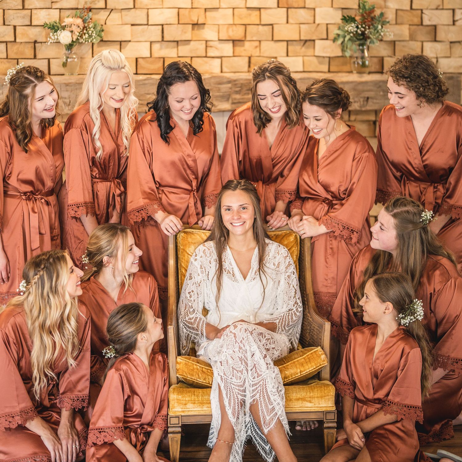 Group photo showing bridesmaids in coral robes sitting together on a yellow bench.