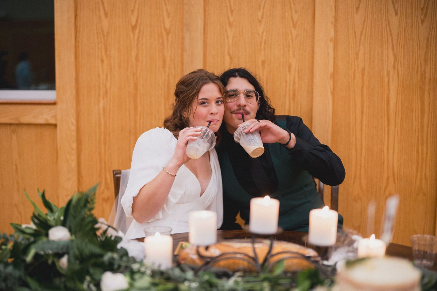 A candlelit table setting with greenery and decorative elements at an indoor celebration.