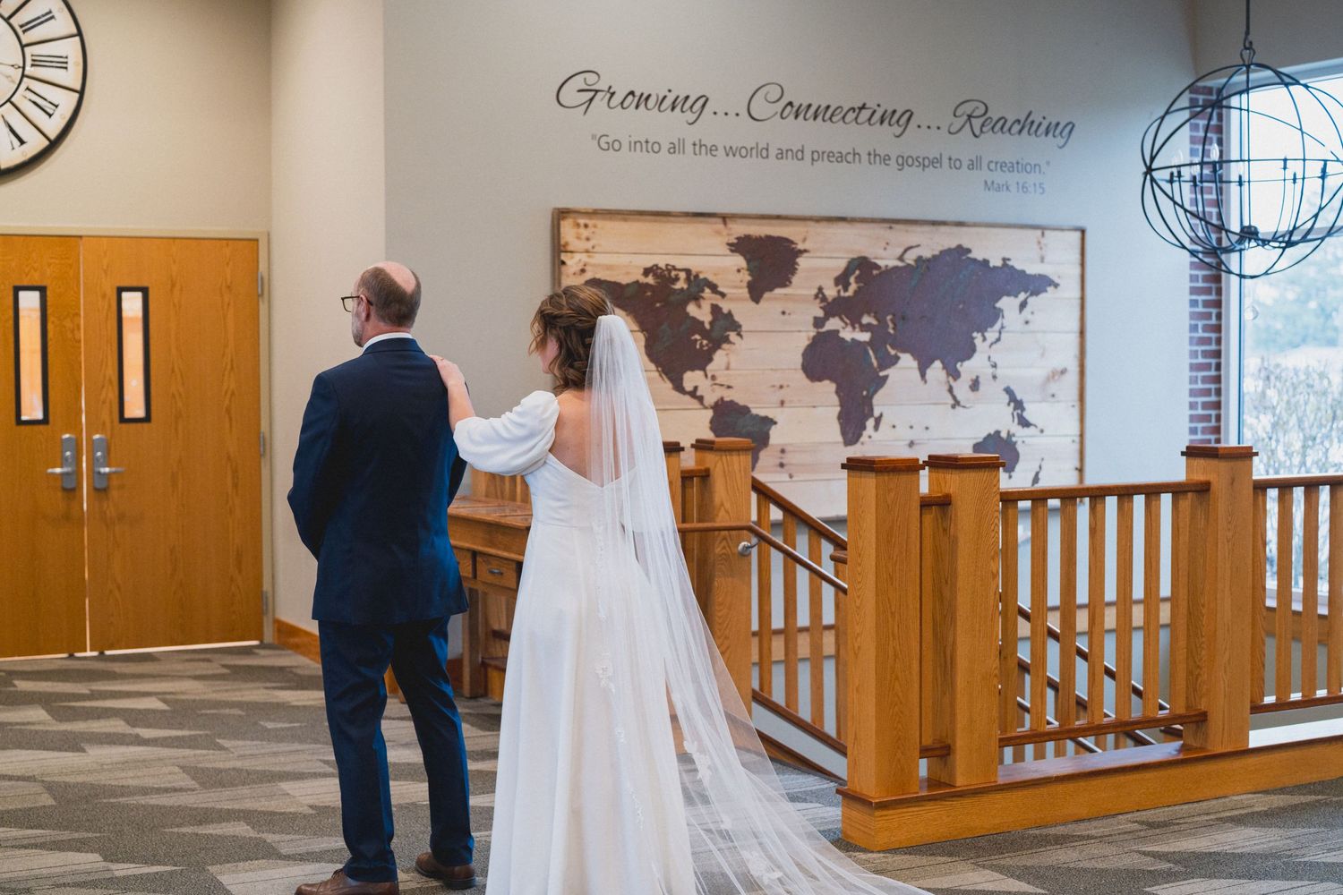 First look wedding moment captured in church hallway with world map wall decor.