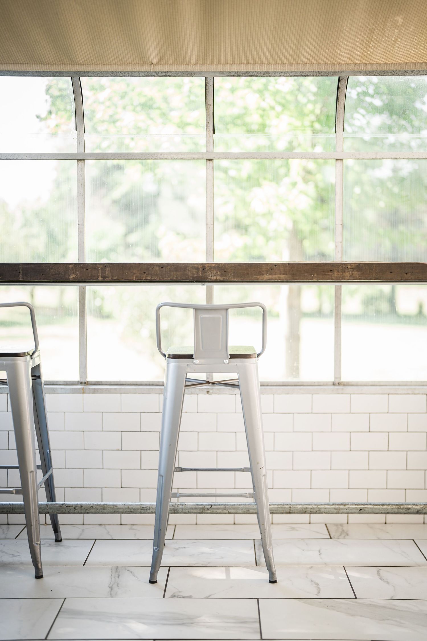 Modern white subway tile wall with industrial style stools and natural lighting through windows.