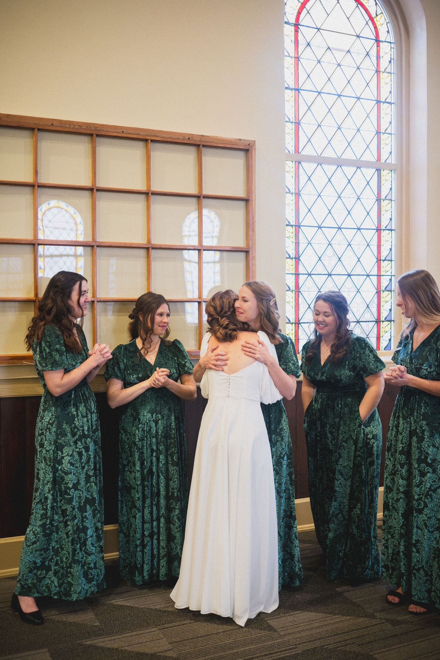 Wedding party in green velvet dresses poses playfully in a church with stained glass windows.