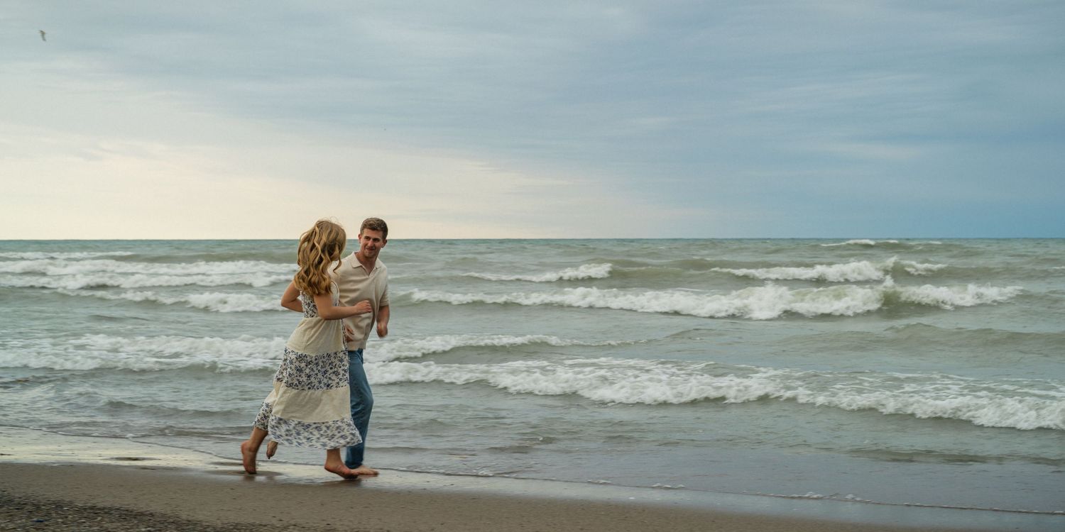 Romantic couple walking hand in hand along a sandy beach with ocean waves at sunset.
