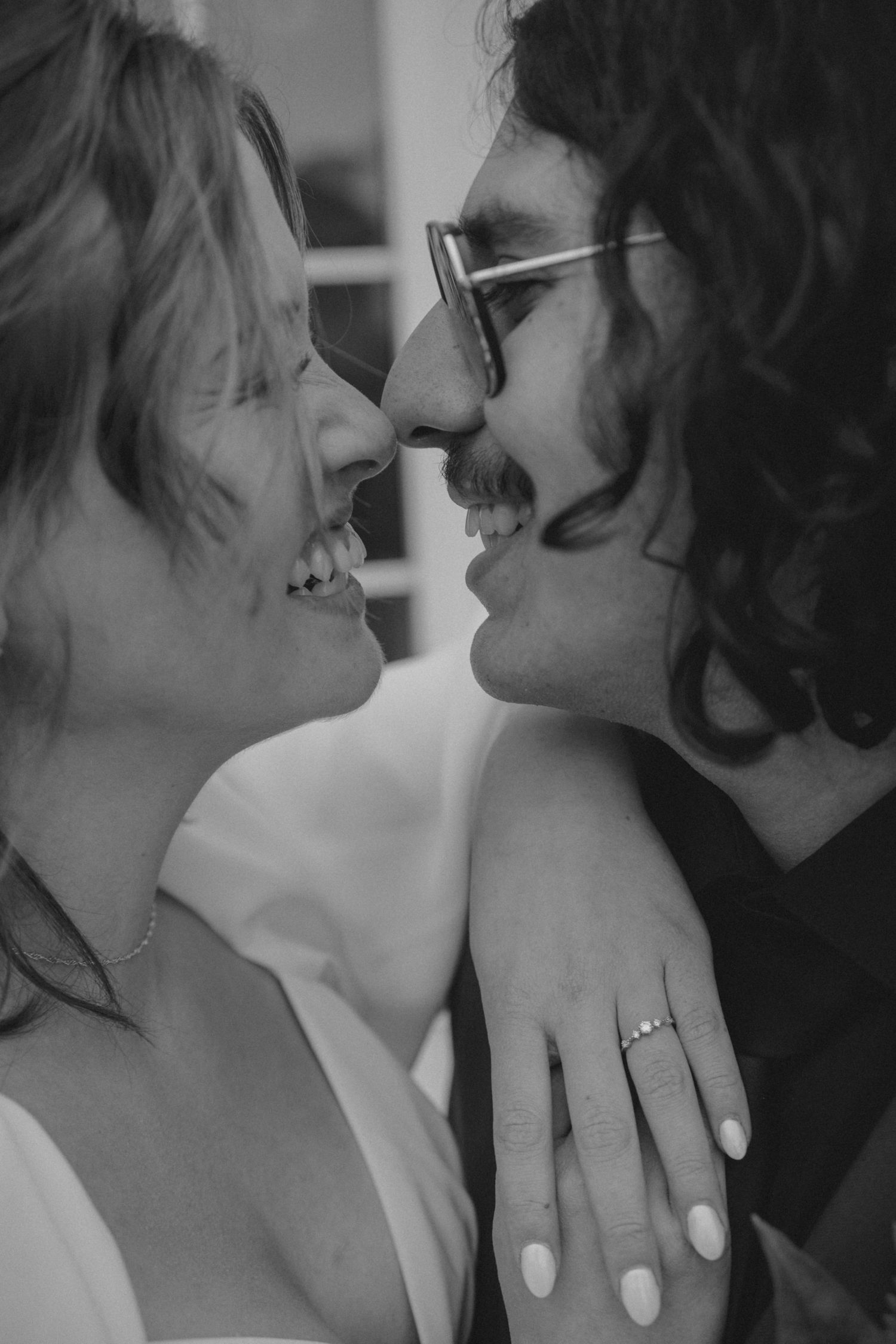 An intimate black and white photo of newlyweds sharing a close moment while showing off the engagement ring.