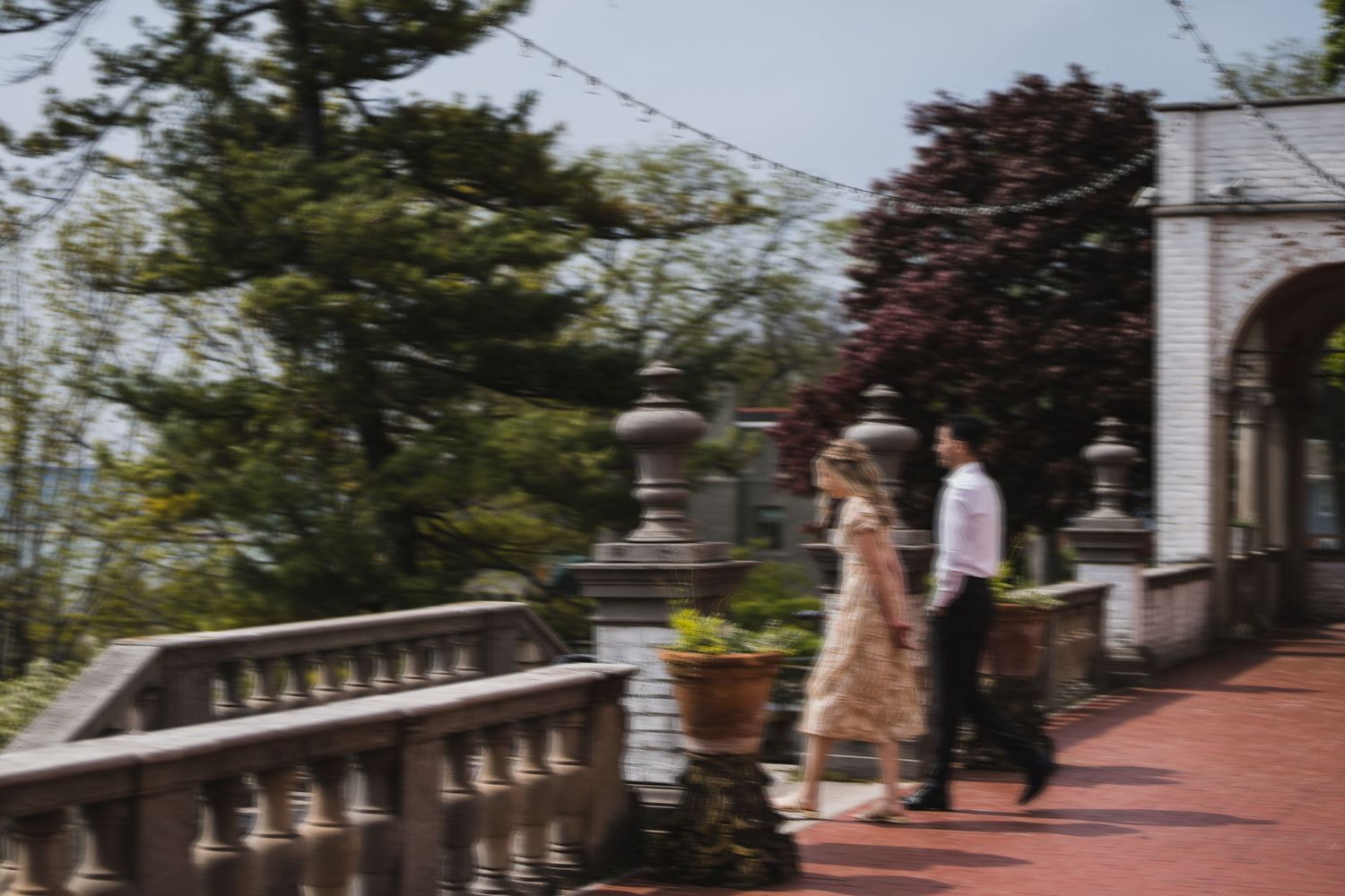 Two people strolling down an elegant brick walkway surrounded by trees and classic architecture.