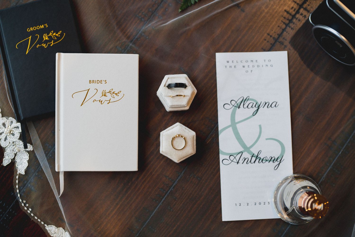 Wedding stationery and ring boxes arranged on a dark wooden surface with gold lettering.