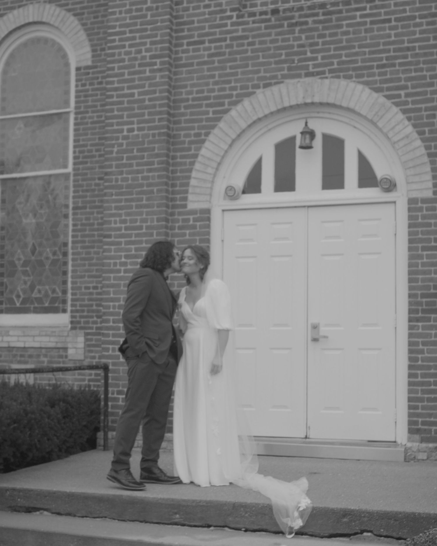 Black and white wedding photos showing intimate moments between a couple at a church entrance.