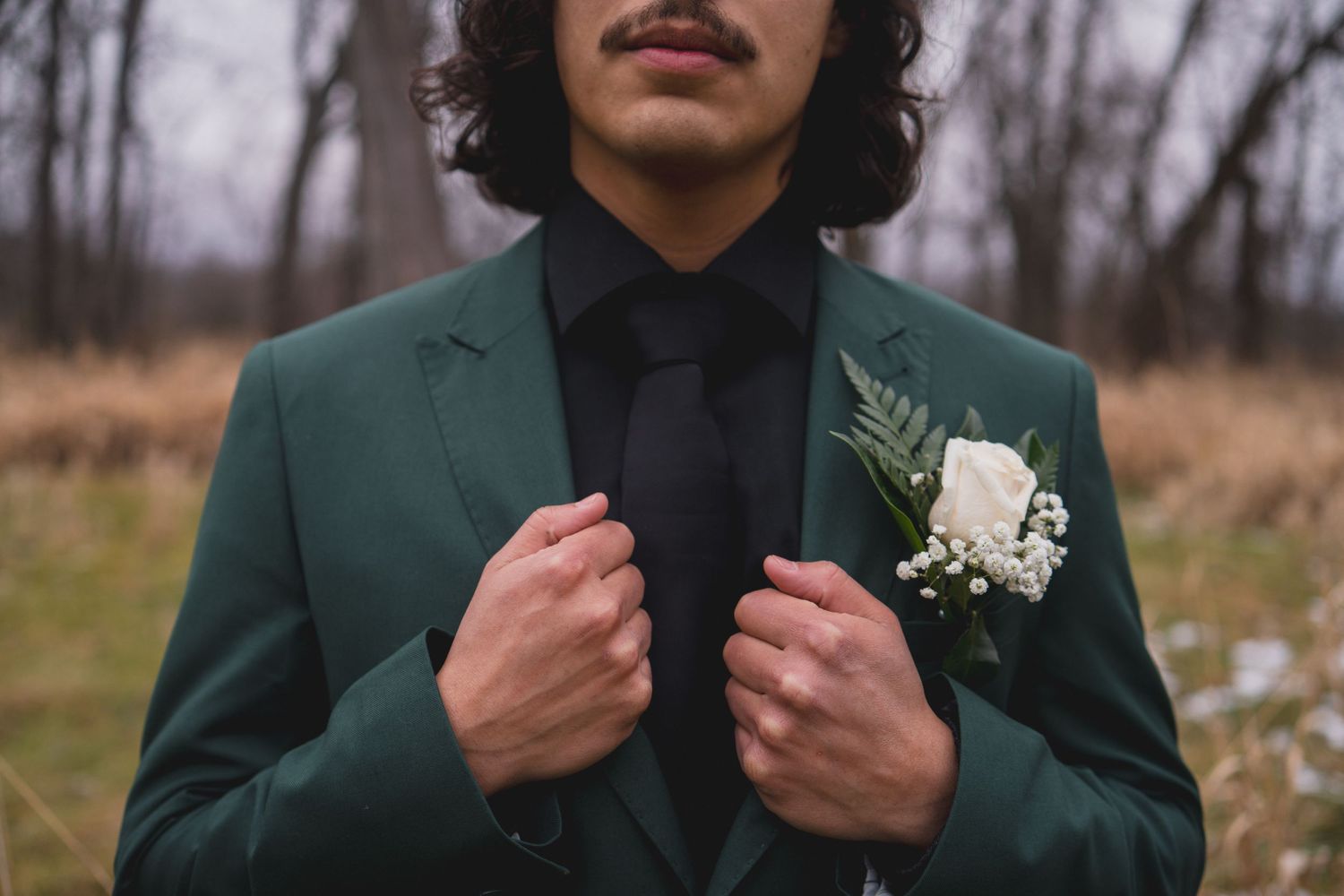 Close-up of emerald green suit jacket with white boutonniere and black shirt.