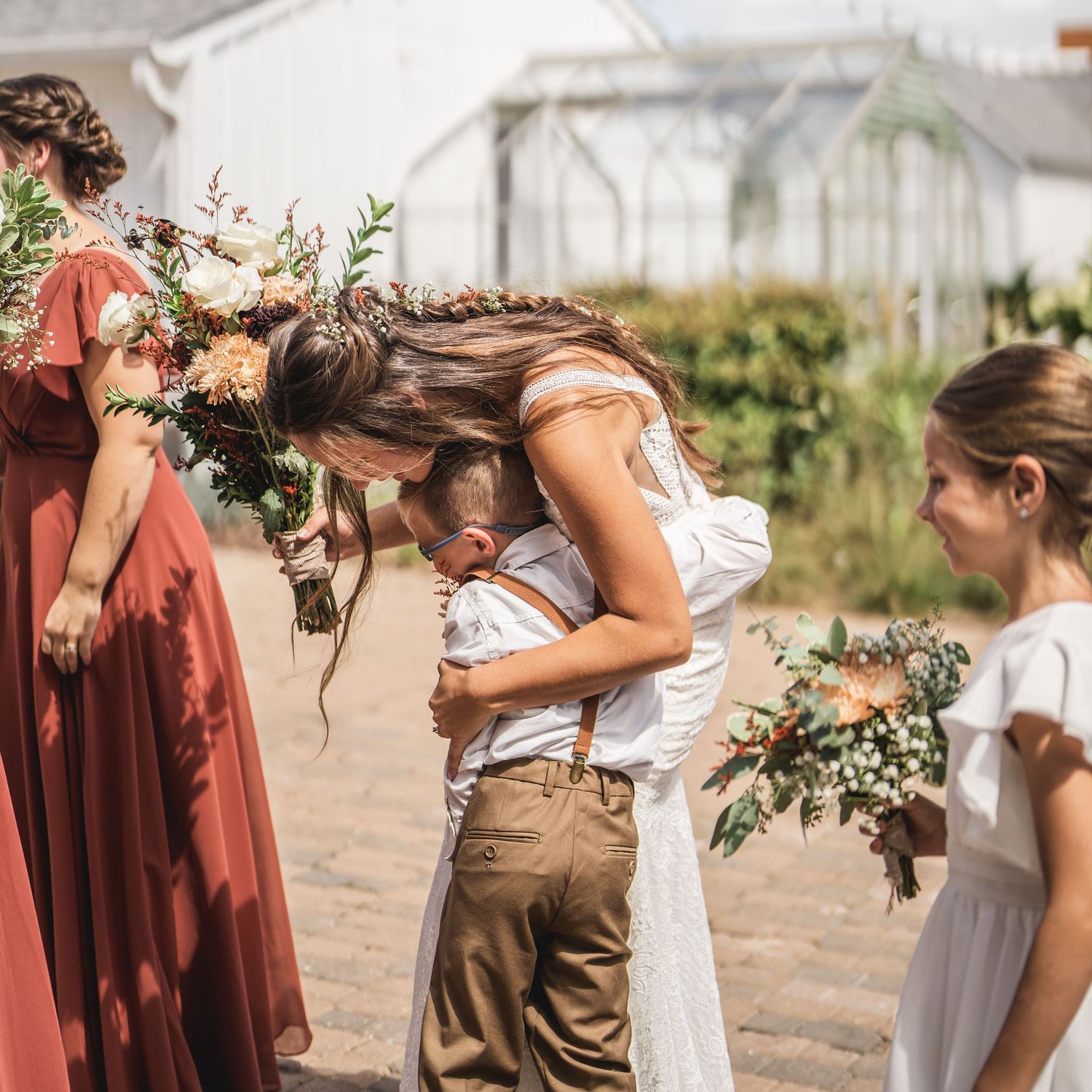 Wedding party members in burgundy and white attire hold floral bouquets.