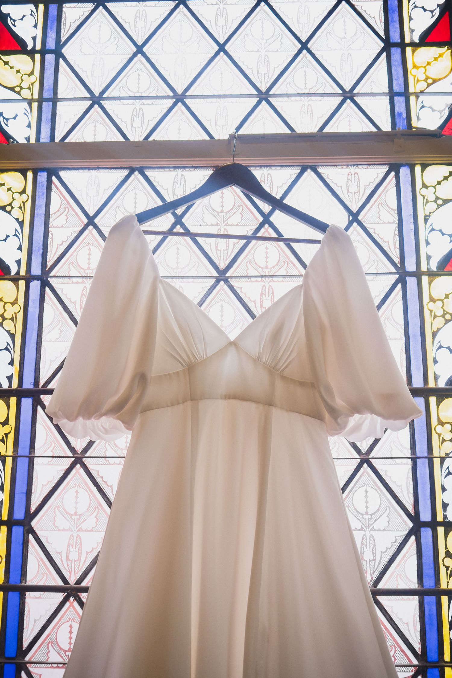 An ethereal wedding gown with puff sleeves displayed against a colorful stained glass window.