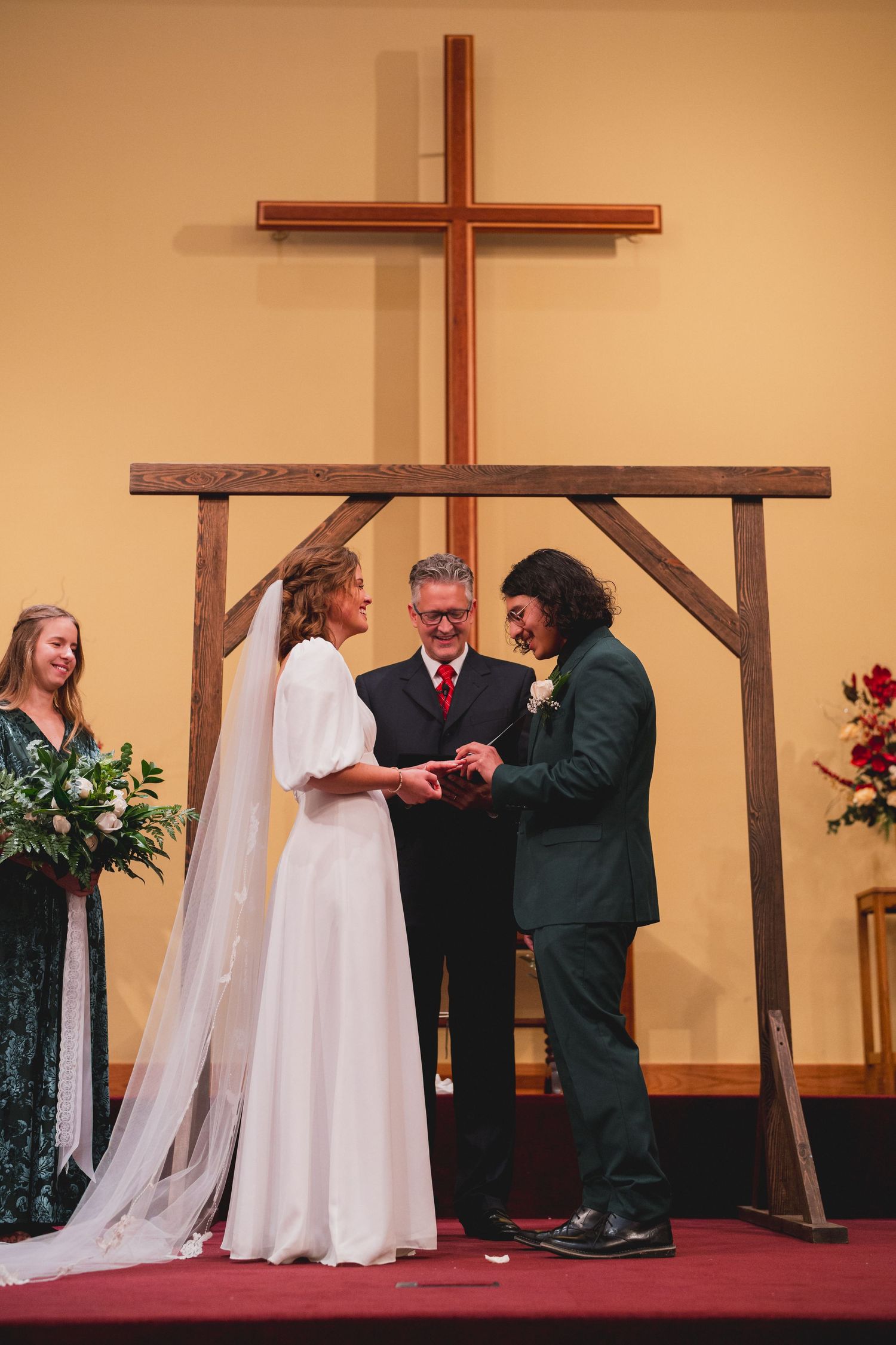 Wedding ceremony under wooden cross with couple exchanging rings as officiant presides.