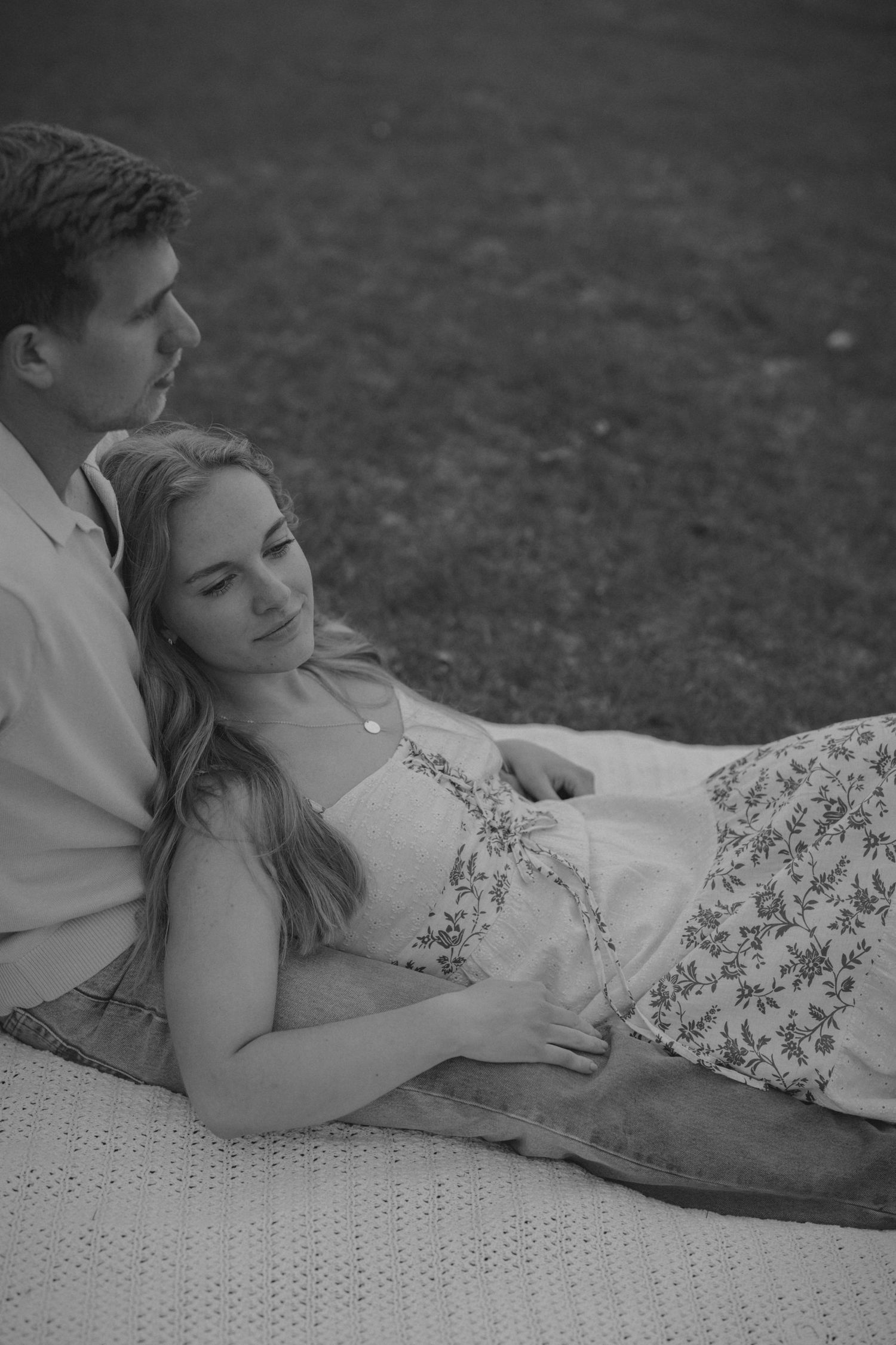 Black and white photo of a couple relaxing on a blanket outdoors, woman resting her head on mans lap.