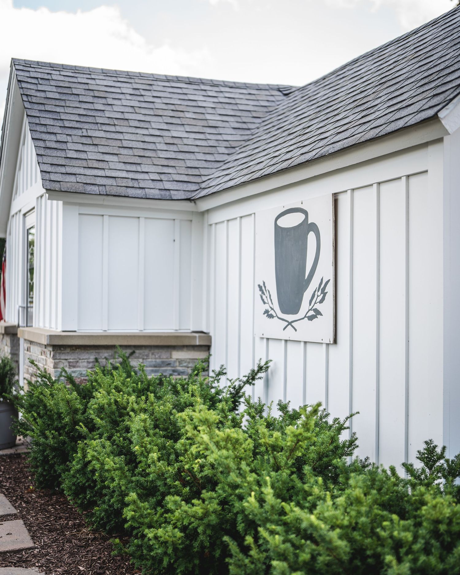 White exterior of a wedding venue with gray shingle roof and manicured green bushes.
