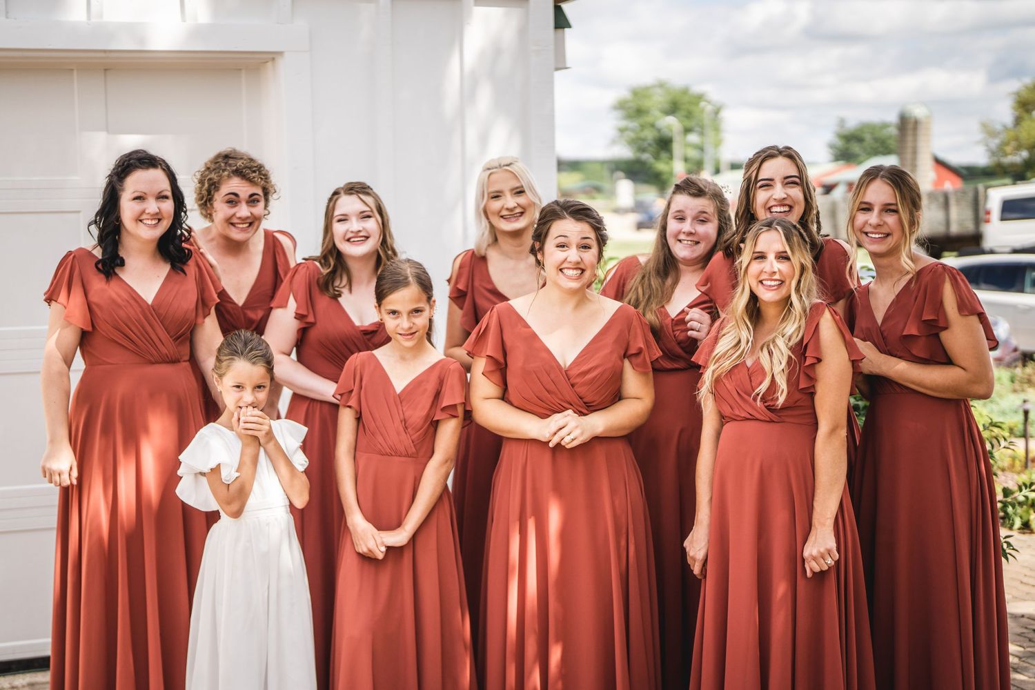 Wedding party members in coordinating rust-colored dresses standing together outdoors.