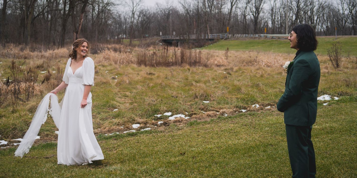 Couple posing outdoors in a field with bare trees and grass on an overcast day.