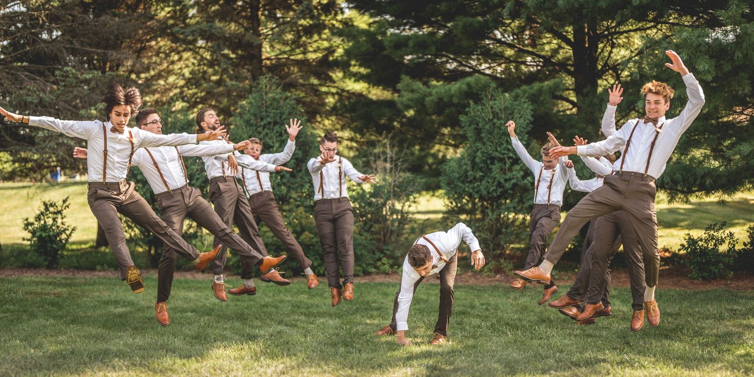 Groomsmen jumping and posing playfully on grass for fun wedding photo.