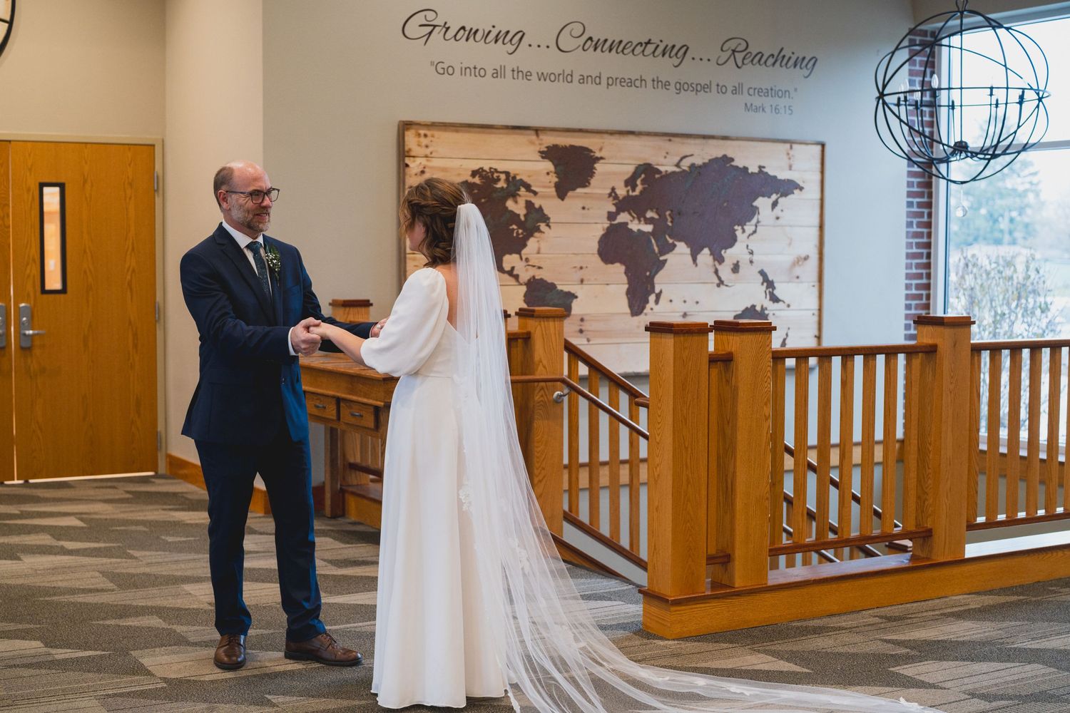 Wedding couple stands together in church hallway with world map and wooden details.