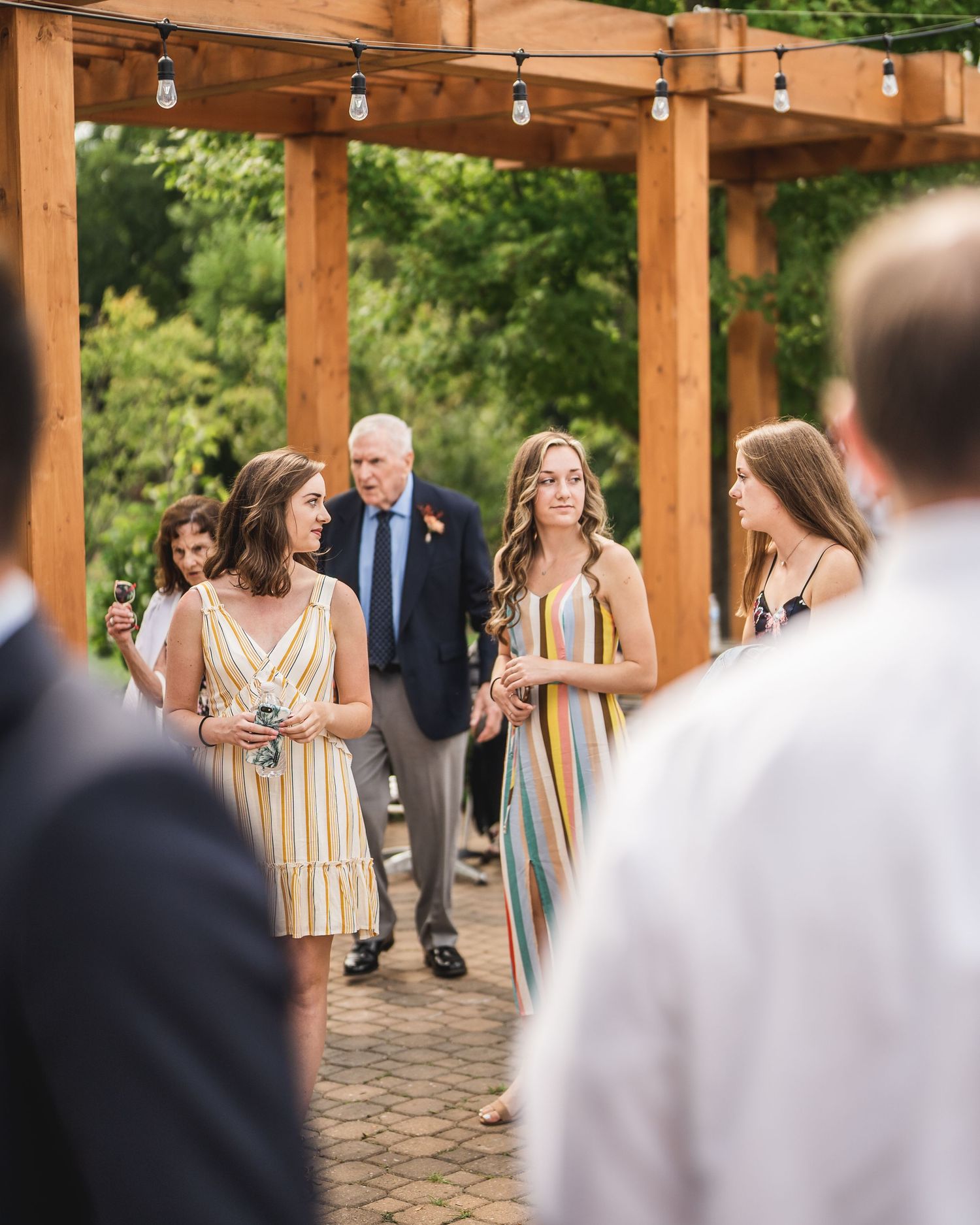 Guests gather under a rustic wooden pergola during an outdoor wedding celebration.