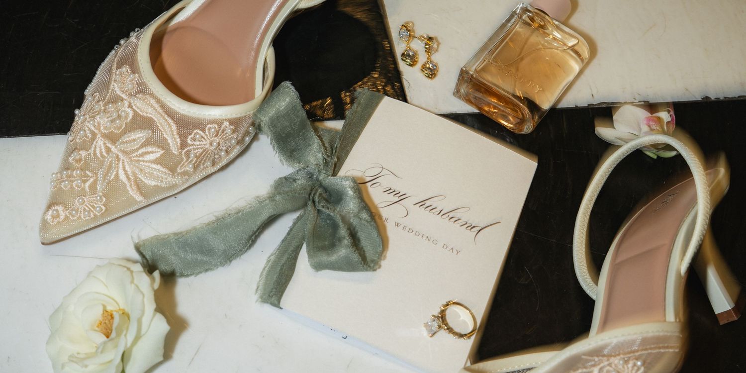 Elegant bridal accessories including embellished shoes, perfume, and wedding stationery on a light surface.