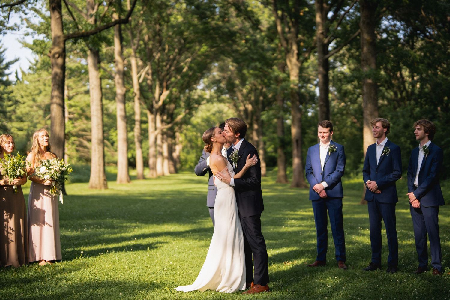 Bride and groom share their first kiss at an outdoor wedding ceremony surrounded by guests.