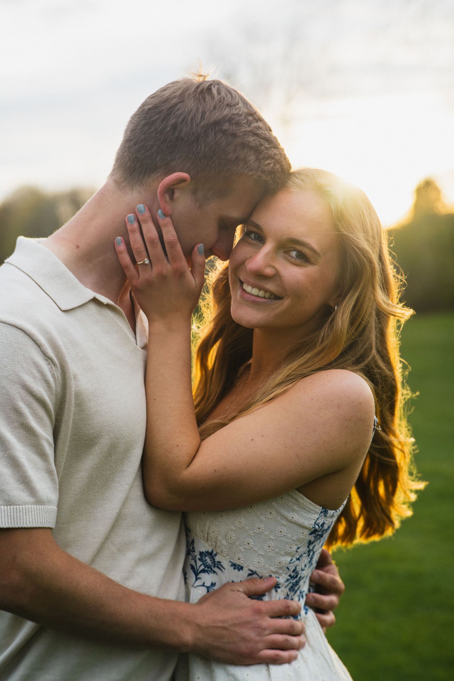 Smiling woman embracing man in golden sunset light on a green field, engagement photo.