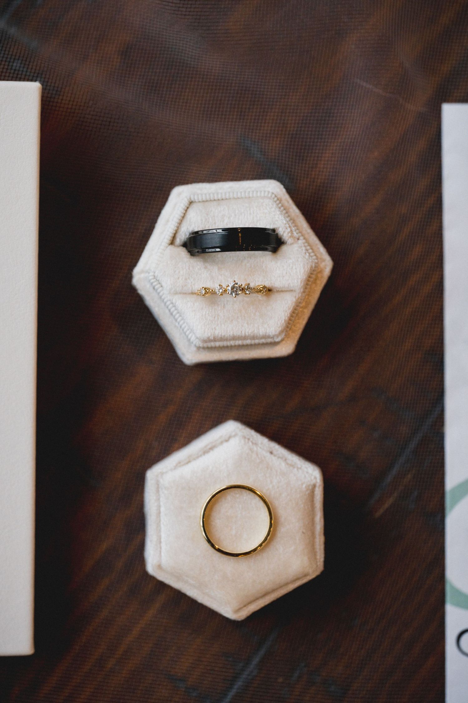 Two hexagonal ring boxes containing wedding bands on a dark wooden surface.