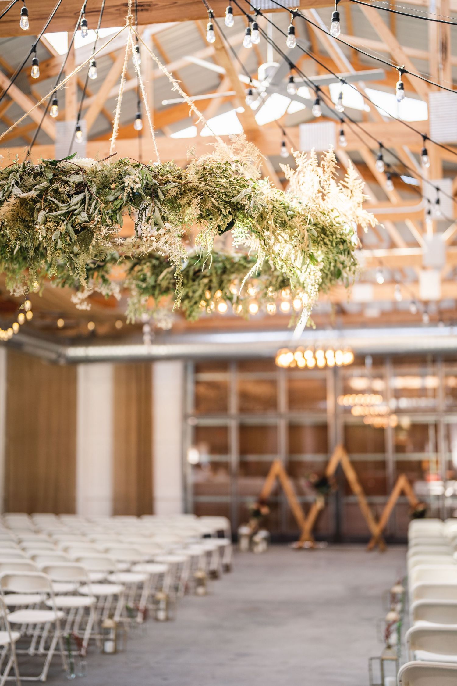 Wedding venue interior with string lights and greenery hanging from wooden beams.