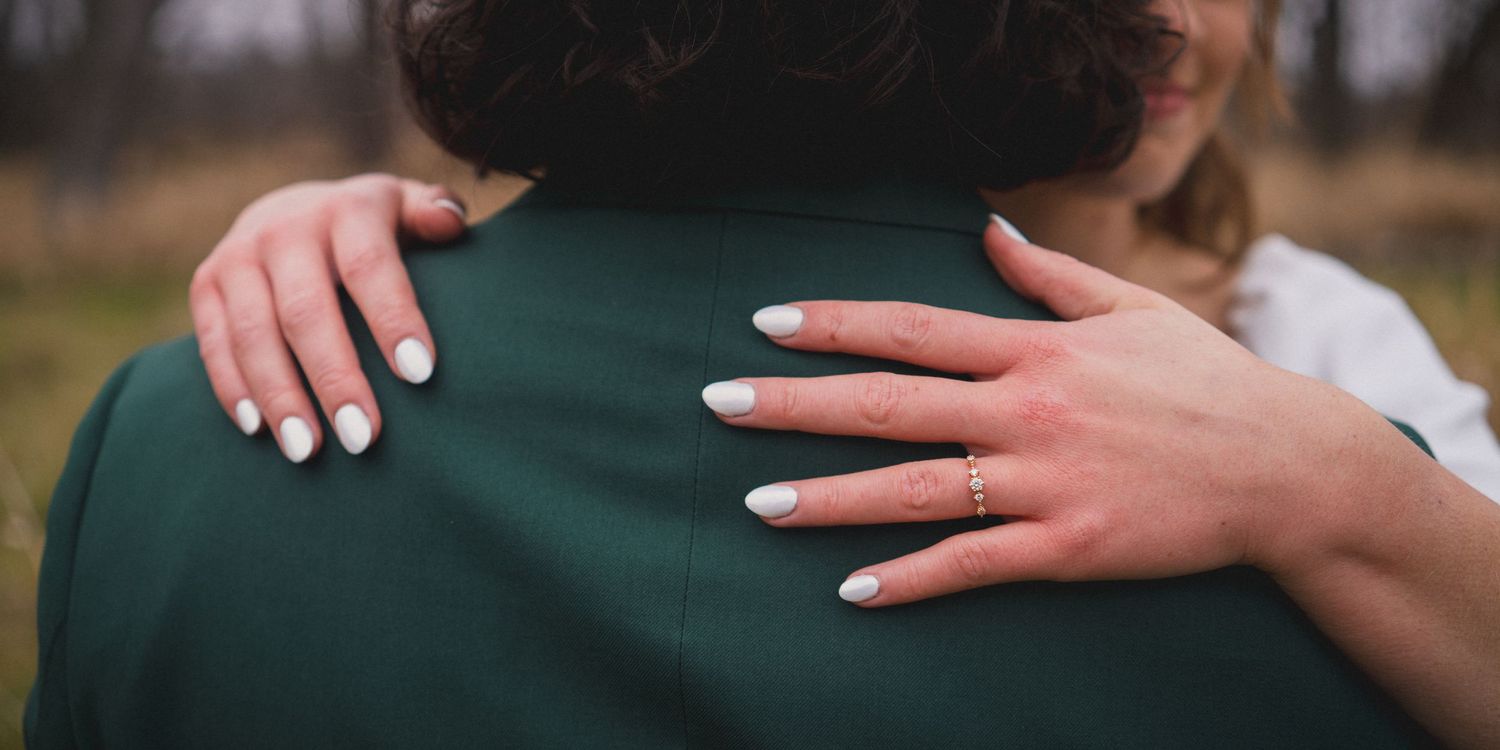 Close-up shot of hands embracing on a green suit jacket during a wedding moment.