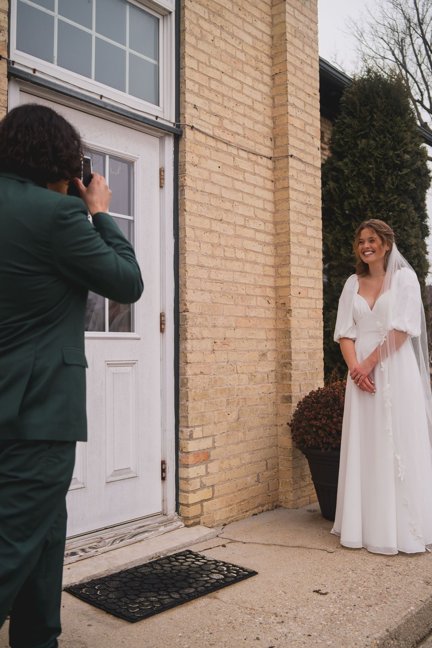 A wedding photoshoot in front of a brick building with photographer capturing the bride's portrait.
