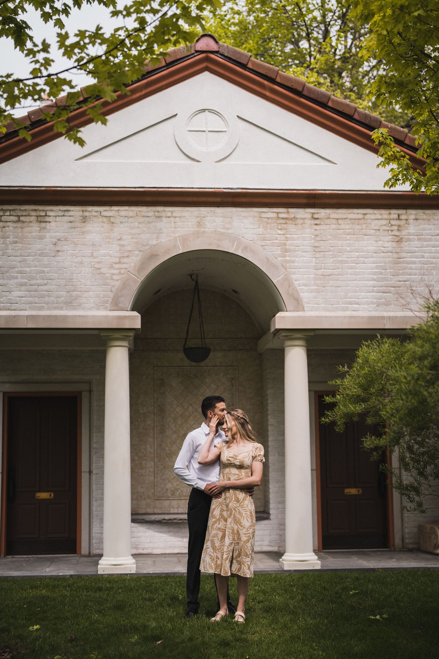 A couple sharing a romantic moment under white columns of a classic building entrance.