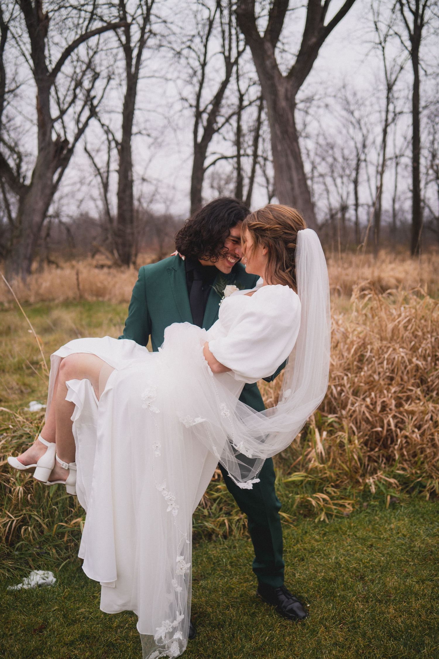 A romantic wedding scene in a field with dried grass and bare trees in winter.