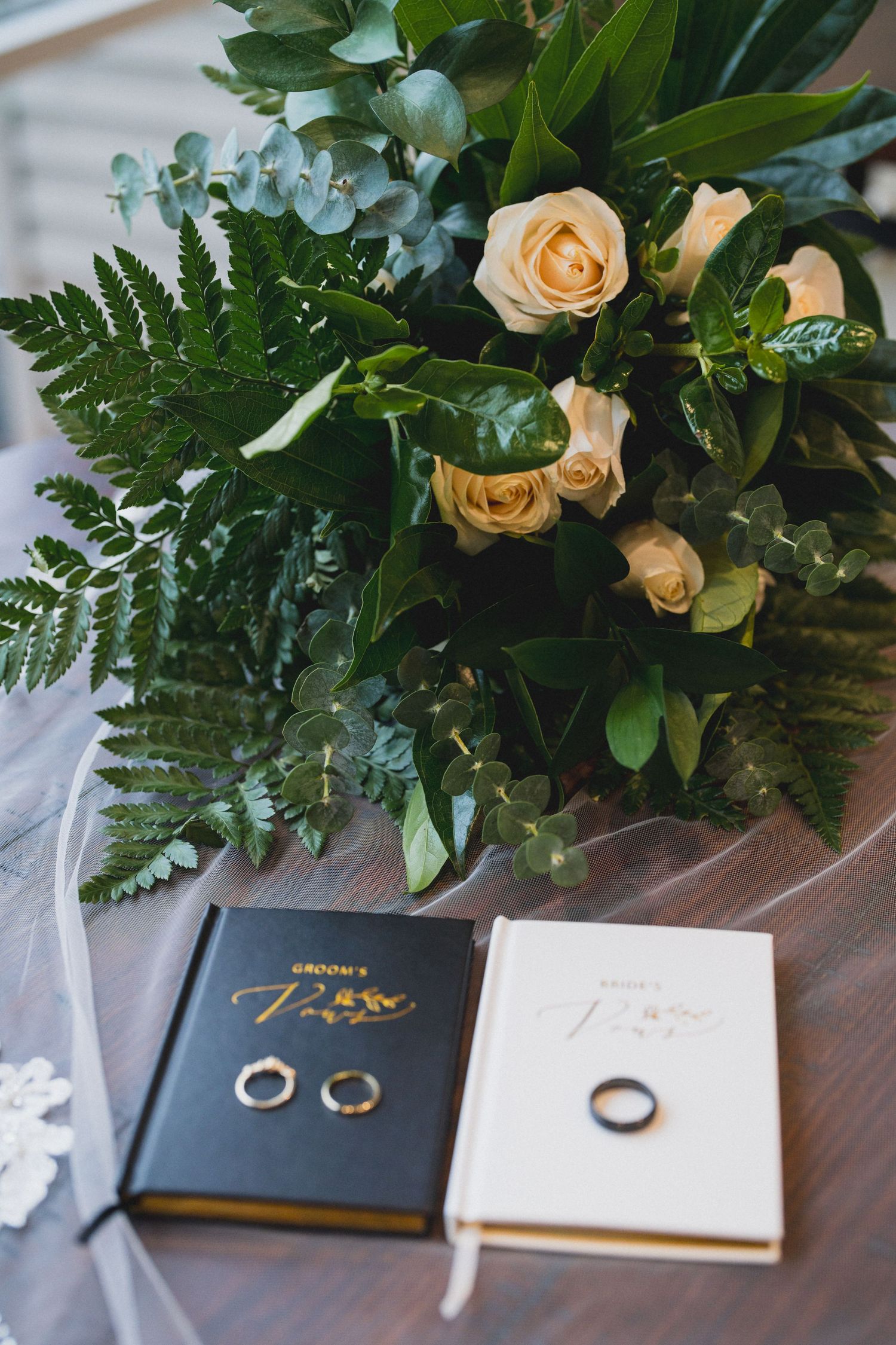 Wedding rings displayed on vow books with peach roses and greenery arrangement.