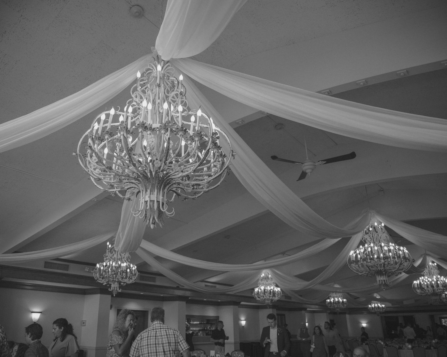 Elegant black and white photo of crystal chandeliers and white draped fabric at wedding venue.